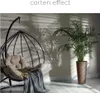 A hanging chair with cushions and a blanket next to a potted plant, with shadows cast on the wall. Náhľad obrázku produktu