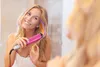 A young woman is styling her hair in front of a mirror with a pink hair straightener. Produktbild-Vorschau