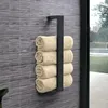 A black metal towel rack with four rolled beige towels hanging on it, mounted on a gray tiled wall. Anteprima dell’immagine prodotto