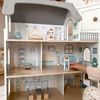 A child's hand is shown interacting with a wooden dollhouse, placing a doll inside. Voir les images du produit