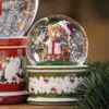 A close-up of a Christmas snow globe with a teddy bear inside, next to another Christmas-themed item. Produktbild-Vorschau