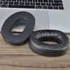 Two black ear pads for headphones are placed on a wooden surface in front of a laptop keyboard. Anteprima dell’immagine prodotto