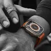 A close-up shot of a person's wrist wearing an Apple Watch Ultra with an orange band. The watch face displays a compass and celestial map. Produktbild-Vorschau