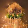 A decorative house-shaped planter filled with artificial flowers and greenery, illuminated by a string of warm white LED lights. Produktbild-Vorschau