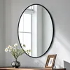 A round mirror with a black frame hangs on a wall above a wooden surface. A vase with white flowers and a small framed picture are on the surface. Podgląd zdjęcia produktu