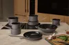 A collection of grey cookware, including pots, pans, and a wok, arranged on a kitchen countertop with a stovetop and cabinets in the background. Produktbild-Vorschau