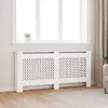 A white radiator cover with a decorative lattice pattern is shown in a room with a window and curtains. Produktbild-Vorschau
