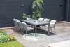 An outdoor dining set with chairs and a table on a patio next to a garden. Produktbild-Vorschau