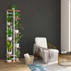 A multi-tiered plant stand filled with various potted plants is placed next to a white armchair with a patterned throw blanket draped over it. A round coffee table with books sits to the right, and a woven basket with towels is on the floor. Podgląd zdjęcia produktu