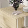 A close-up view of a wooden table with a folded napkin, a vase of purple flowers, and a stack of white plates. Produktbild-Vorschau
