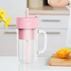 A pink and clear electric blender with a straw, placed on a white surface next to sliced oranges on a wooden cutting board. A child's hand is visible in the upper right corner. Produktbild-Vorschau