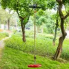 A zipline kit with a red disc seat hanging from a cable between two trees in a grassy, wooded area. Produktbild-Vorschau