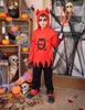 A child dressed in a devil costume for Halloween, holding a trident, with Halloween decorations in the background. Produktbild-Vorschau