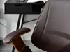 A close-up view of a brown leather office chair armrest and part of the backrest, with a black desk in the background. Produktbild-Vorschau