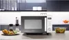 A modern kitchen scene featuring a microwave, a baked potato with salad, and a bowl of salad. Produktbild-Vorschau