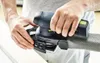 A person's hands are holding and operating a sander on a piece of wood. Voir les images du produit