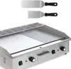 A stainless steel electric grill with two spatulas shown above it, against a white background. Náhled obrázku produktu