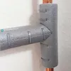 A close-up view of a grey pipe insulation fitting with copper pipes visible. Produktbild-Vorschau