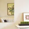 A living room scene with a sofa, a painting, and a shelf with a plant and a framed picture. Produktbild-Vorschau