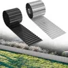 Two rolls of corrugated metal garden edging, one black and one silver, are shown unrolled and installed along a garden bed. The background depicts a garden with grass, plants, and a hint of a fence or structure. Voir les images du produit