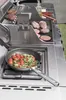 A close-up shot of a premium BBQ kitchen with food being cooked on the grill and in a pan. Produktbild-Vorschau