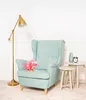 A plush dinosaur toy sits on a light blue armchair next to two small side tables with decorative items. Voir les images du produit