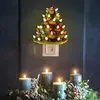 A ceramic Christmas tree night light plugged into a wall socket, with candles and greenery below. Náhľad obrázku produktu