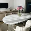 A dining table with chairs, decorated with a vase of hydrangeas, in a bright, modern living room setting with sunlight streaming through. Produktbild-Vorschau