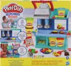 The image shows the packaging of a Play-Doh Kitchen Creations Busy Chef's Restaurant Playset. It features colorful illustrations of the playset, Play-Doh containers, and food items, along with images of children playing with the toy. Náhľad obrázku produktu
