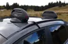 Two ski/snowboard carriers are mounted on the roof of a car, parked in a grassy, hilly area with trees in the background. Produktbild-Vorschau