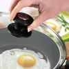 A hand is holding the handle of a pot lid, with a fried egg cooking in the pot below. Anteprima dell’immagine prodotto