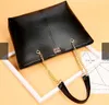 A black leather handbag with gold chain straps is displayed on a light yellow and white background, with some paper elements in the background. Náhľad obrázku produktu