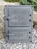 A cast iron oven door with decorative elements, placed outdoors on gravel and rocks. Náhľad obrázku produktu