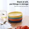 A stack of colorful plates on a wooden table next to a glass of water. Produktbild-Vorschau