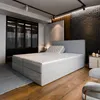 A bedroom scene featuring a large bed with a headboard, mattress, and topper. The room has a modern and luxurious feel with a large wardrobe, textured wall, and wooden flooring. Produktbild-Vorschau