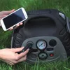 A person is using a portable power station to charge a smartphone and possibly inflate a tire, outdoors on grass. Podgląd zdjęcia produktu