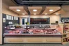 A well-lit butcher shop display counter filled with various meats and sausages, with hanging sausages visible in the background. Produktbild-Vorschau