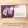 An open booklet with an illustration on the left page and text on the right page, placed on a wooden surface. Produktbild-Vorschau