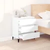 A white three-drawer dresser is placed next to a wooden bed frame in a bedroom setting. Podgląd zdjęcia produktu