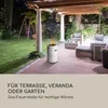 A gas fire pit is shown on a wooden deck in a garden setting at dusk, with furniture and plants visible. Produktbild-Vorschau