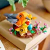 A LEGO Creator bird's nest set with three toy birds and eggs, placed on a cardboard box with some greenery in the background. Produktbild-Vorschau