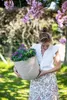 A woman is holding a potted plant in a garden setting. Náhľad obrázku produktu