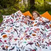 Two children are lying in a bed with a patterned duvet outdoors. Produktbild-Vorschau