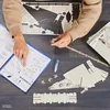 A person's hands are assembling a 3D puzzle of the Millennium Falcon, with instructions open on the table. Anteprima dell’immagine prodotto