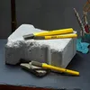Three yellow chisels are placed on a large gray stone block, with smaller stone fragments in the foreground. Anteprima dell’immagine prodotto