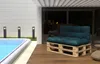An outdoor patio scene with a swimming pool and a pallet sofa. Voir les images du produit