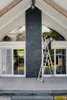 A person is cleaning a large window on a modern house with a ladder. Produktbild-Vorschau
