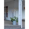 Two LED decorative spheres with lights are placed in a planter filled with white flowers on a porch. Produktbild-Vorschau