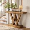 A wooden console table with a V-shaped base is placed in a hallway next to a staircase. A vase with greenery, a lamp, and books are on the table. Podgląd zdjęcia produktu