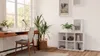 A bright, modern room with a desk, chair, and a cube shelf filled with decorative items and books, next to a large window. Produktbild-Vorschau